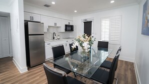 A modern kitchen with white cabinetry, a stainless steel refrigerator, a microwave, and a glass dining table with chairs. - El Mar Escape Condo Lauderdale-by-the-Sea 114 (Lauderdale-by-the-Sea)