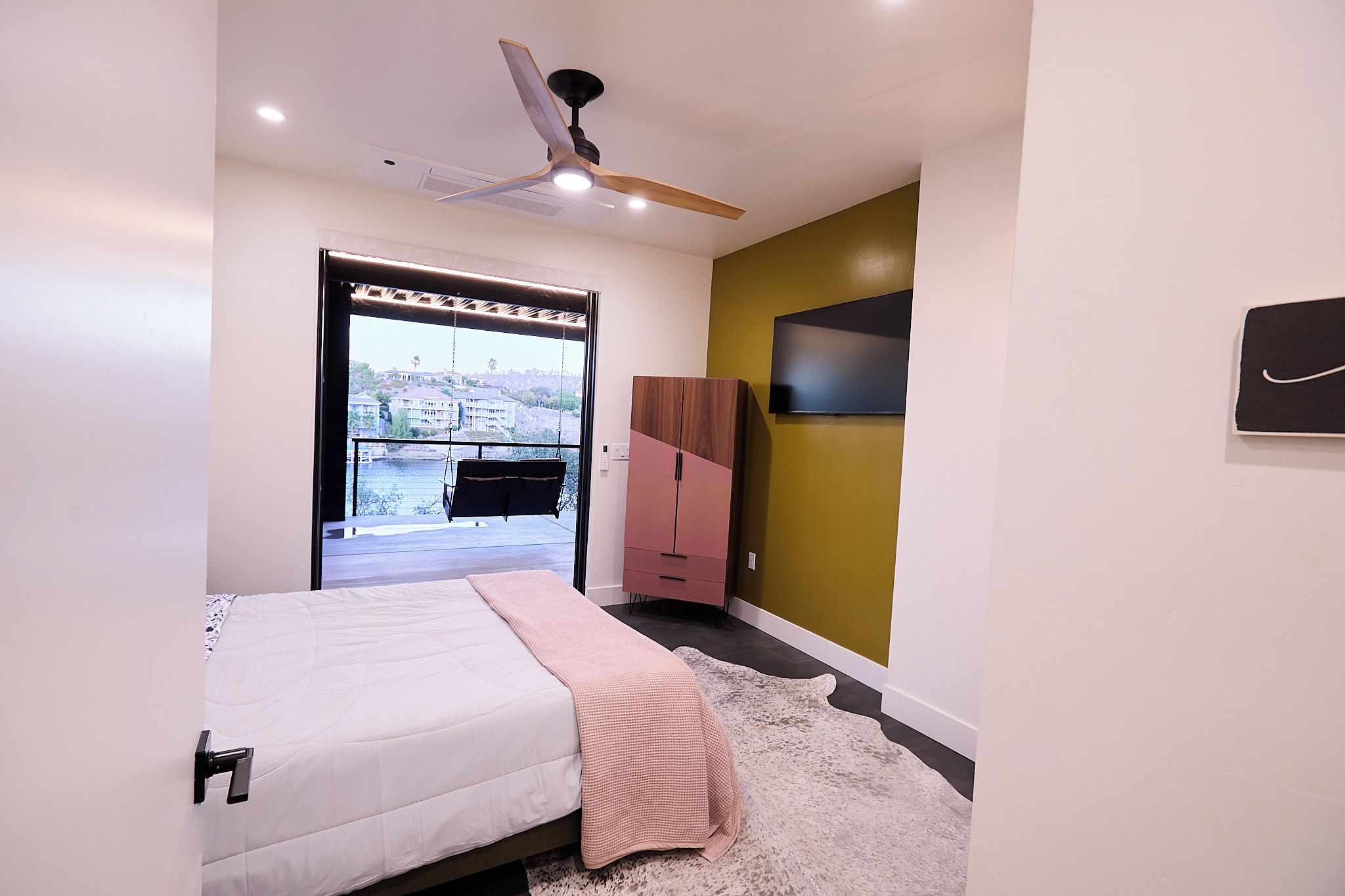 A bedroom with a bed, a wardrobe, a television, and a view of a balcony.