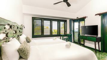 A hotel room with two beds, a ceiling fan, a TV on a stand, a window with shutters, and a green door.