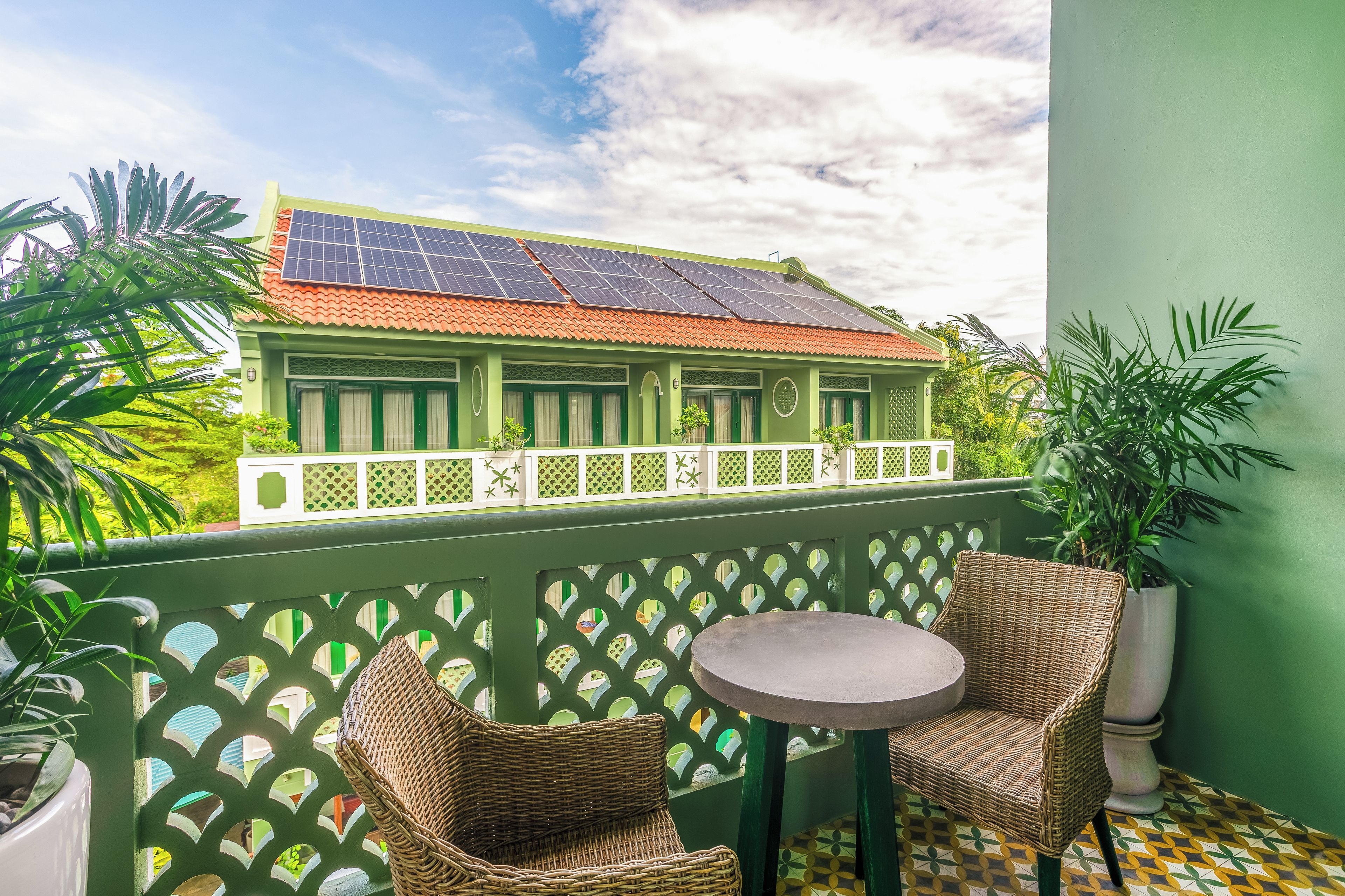 Varanda com cadeiras de vime, uma mesa pequena e vista para um edifício com painéis solares.