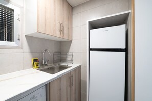 A modern kitchen with a stainless steel sink, wooden cabinets, and a white refrigerator. - GuestReady - Urban Studio in Barrio del Pilar (Madrid)