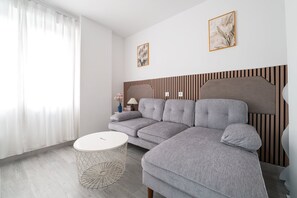 A modern living room with a sectional sofa, a round coffee table, and a decorative mirror. - GuestReady - Urban Studio in Barrio del Pilar (Madrid)