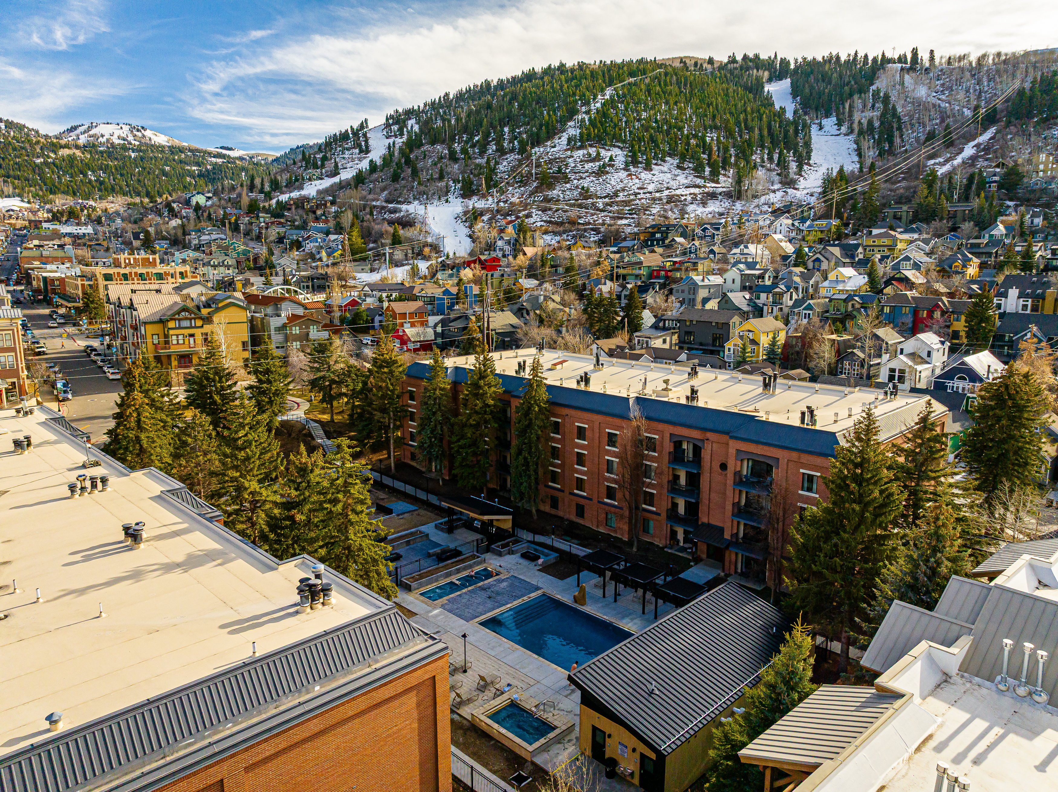 Une ville où se côtoient des bâtiments résidentiels et commerciaux, avec une piste de ski en arrière-plan et un espace piscine.