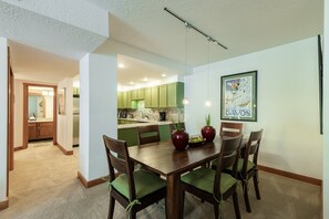 A dining area with a wooden table and chairs, a kitchen in the background, and a framed picture on the wall. - Historic Old Town condo with ski access, pool, hot tub, and mountain views. (Park City)