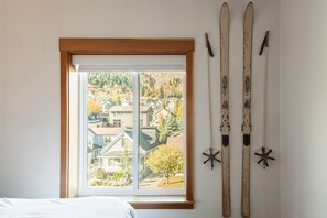 Un dormitorio con ventana que da a una zona residencial, una cama y dos pares de esquíes colgados en la pared.