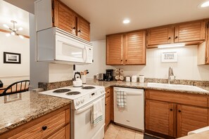 A kitchen with wooden cabinets, a white microwave, a stove, and a dishwasher. - Historic Old Town 2BR/2BA condo with hot tub, pool, sauna & walk-to-lift access. (Park City)