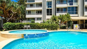 A swimming pool with a curved edge, surrounded by a hedge and trees. - Lvl 32- Ocean Views -Sleeps 6- Parking (Surfers Paradise)