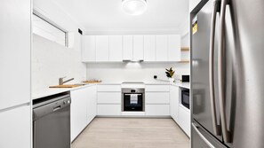 Modern white kitchen workspace equipped with sleek cabinetry, a built-in oven, range hood, and stainless steel appliances. - Lvl 32- Ocean Views -Sleeps 6- Parking (Surfers Paradise)