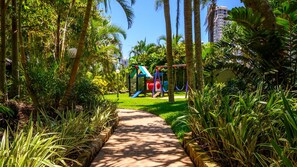 A pathway leading to a playground with slides and swings, surrounded by lush greenery and palm trees. - Lvl 32- Ocean Views -Sleeps 6- Parking (Surfers Paradise)