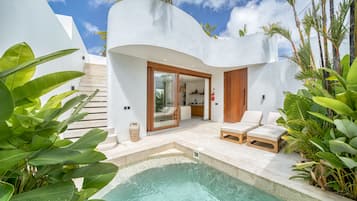 Un área de piscina moderna al aire libre con un edificio blanco curvo, una puerta de madera y un espacio de descanso con dos sillones de jardín.