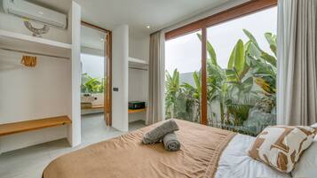 Un dormitorio moderno con una cama grande, un estante de madera y vistas a plantas tropicales a través del ventanal.