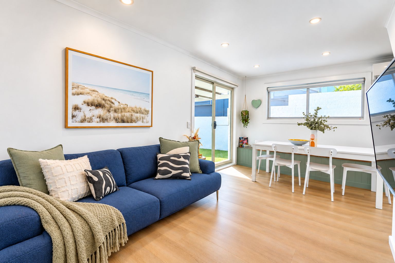 Un salon moderne avec un canapé bleu, une table à manger avec des chaises blanches et une grande fenêtre donnant sur l’extérieur.