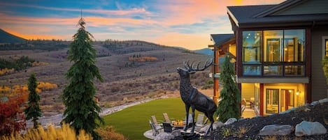 A modern house with a large glass window, a deer statue, and a view of a valley.