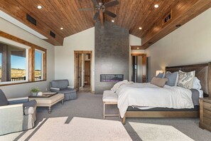 Een slaapkamer met een groot bed, een open haard, een plafondventilator en uitzicht op de omgeving.