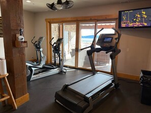 A gym with treadmills, stationary bikes, and a television displaying a game. - Summit Lakehouse -   Luxe Home, Sleeps 39, Game Room, Yard, Fire Pit! (Fish Haven)