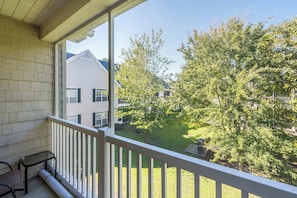A balcony with a view of a residential area, a small table, and a chair.