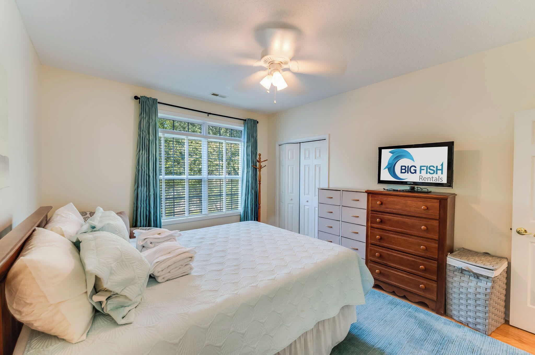 A bedroom with a bed, a dresser, a television, and a window with curtains.