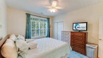 A bedroom with a bed, a dresser, a television, and a window with curtains.