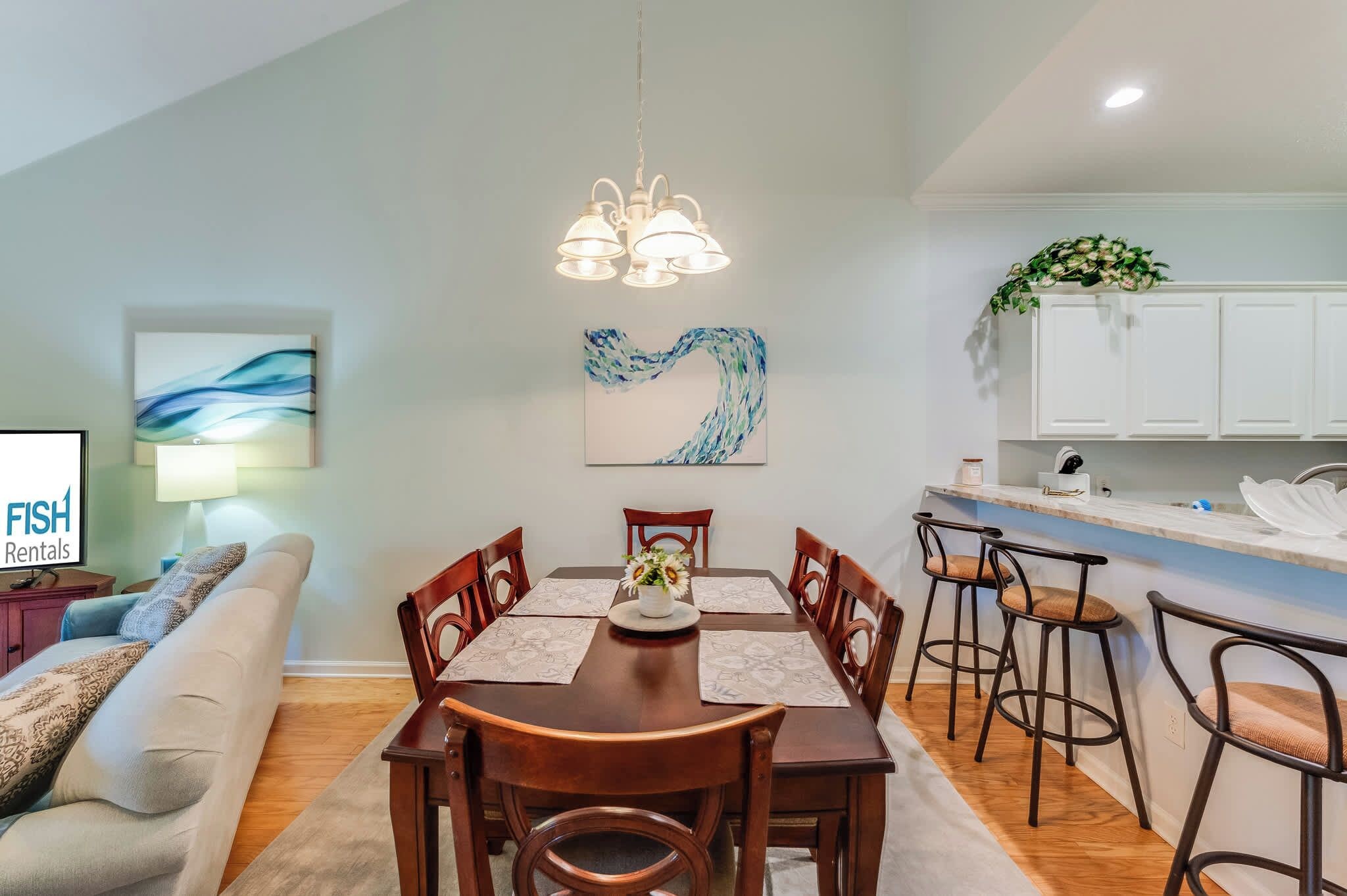 A modern living room with a dining area, a kitchen, and a TV displaying 'FISH Rentals'.