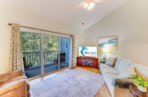 Un salon comprenant un canapé, un téléviseur, un meuble en bois et une porte-fenêtre coulissante donnant sur un balcon.