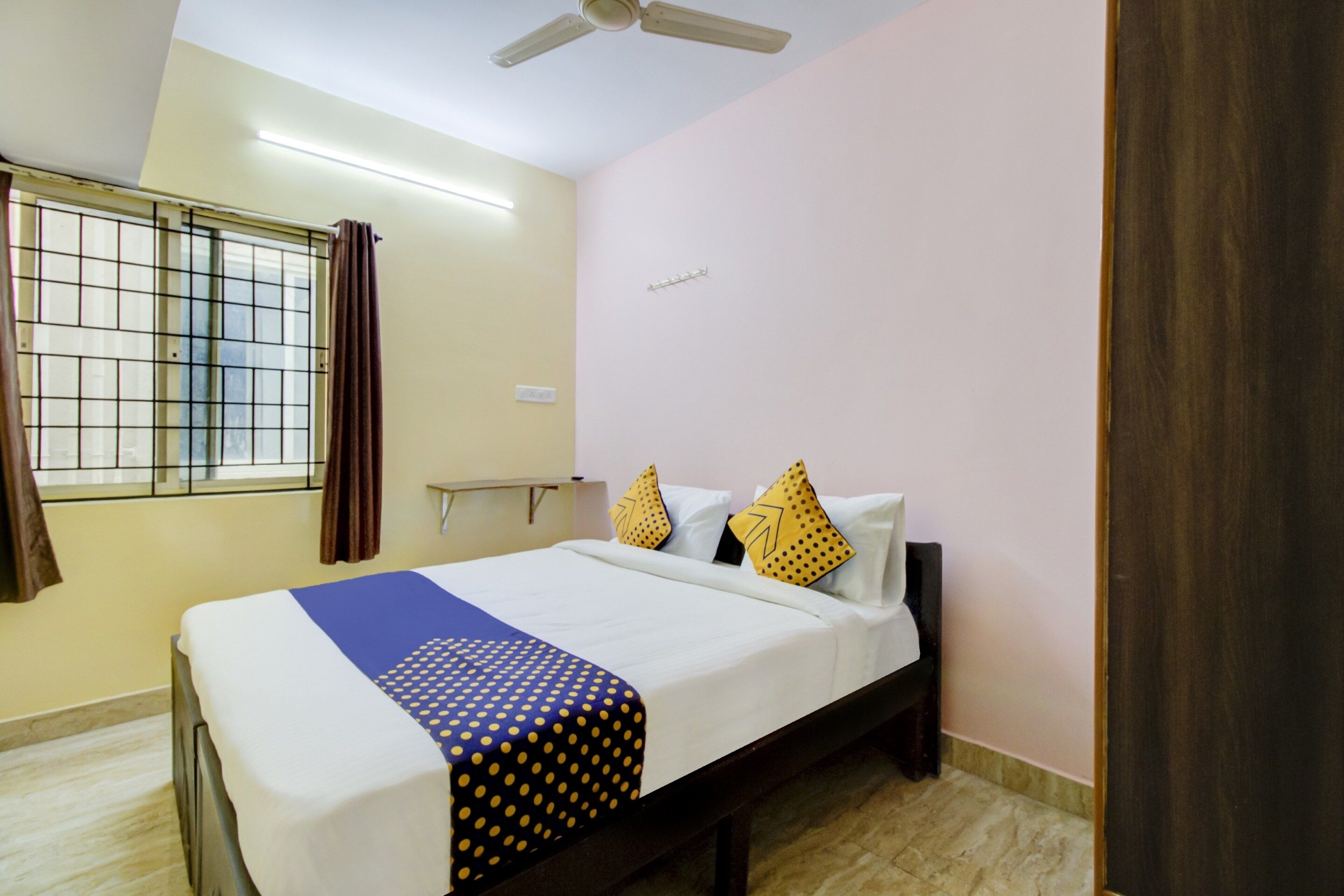 Habitación de hotel con cama, ventana con cortinas, ventilador de techo y lámpara en la pared.