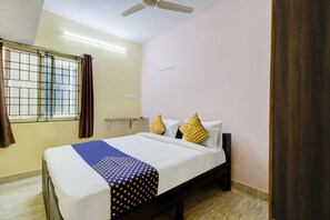 A hotel room with a bed, a window with curtains, a ceiling fan, and a wall-mounted light fixture. - Hotel O Manyata Deluxe (Bangalore)