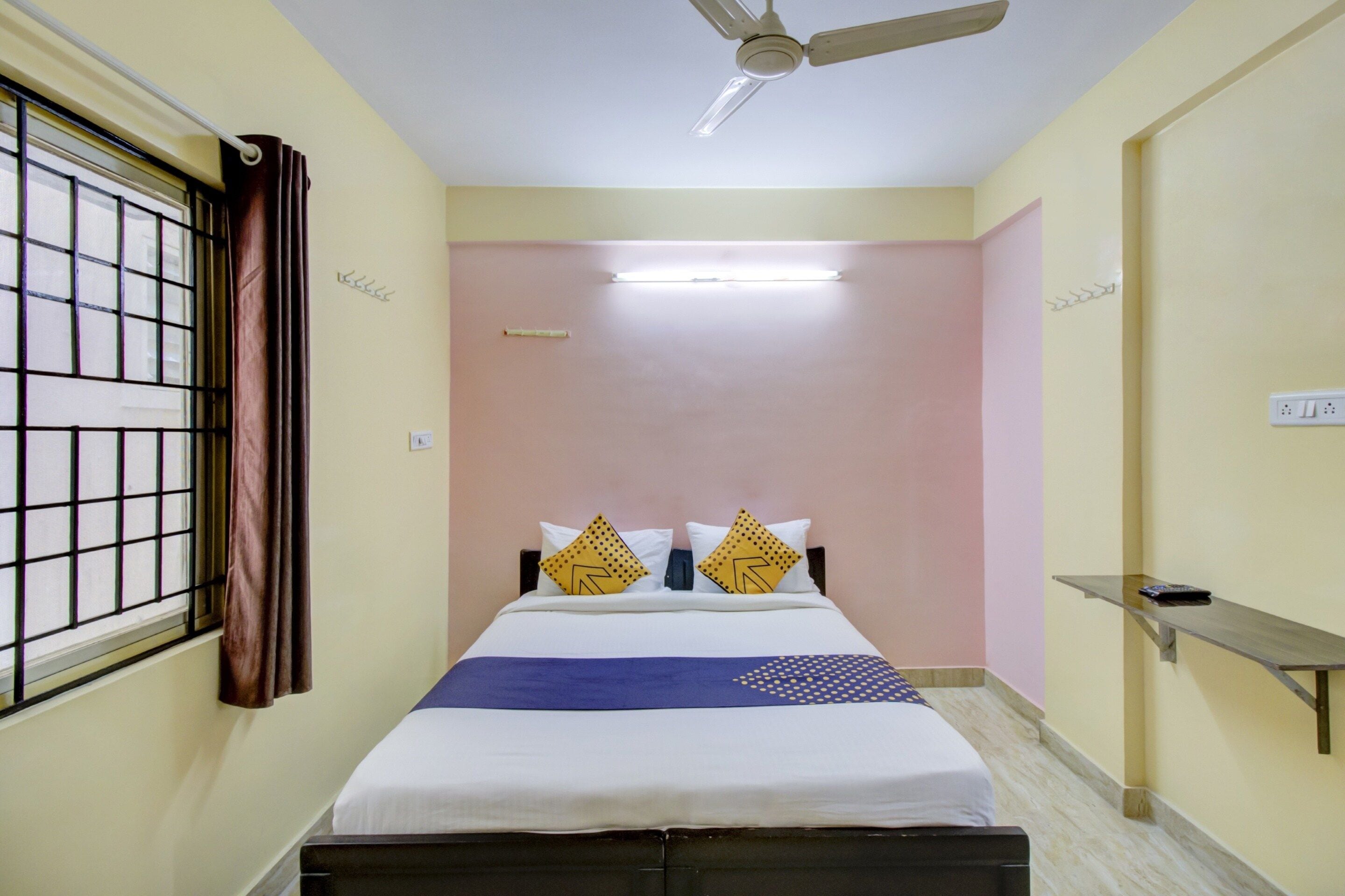 Une chambre d’hôtel avec un lit, un ventilateur de plafond, une fenêtre avec des rideaux et une table de chevet.