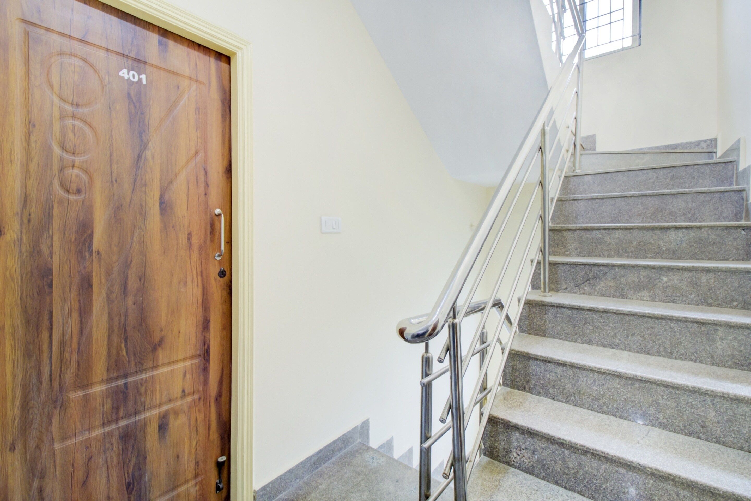 Une porte en bois avec une plaque portant un numéro, un escalier avec des rampes en métal et un interrupteur sur le mur.