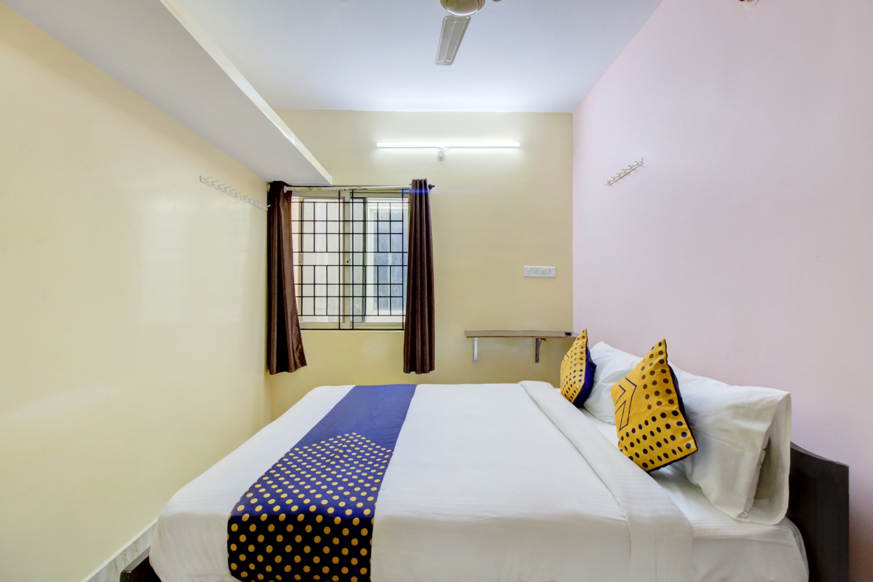 Habitación de hotel con cama, cortinas, ventana con rejas, ventilador de techo y mesita de noche.