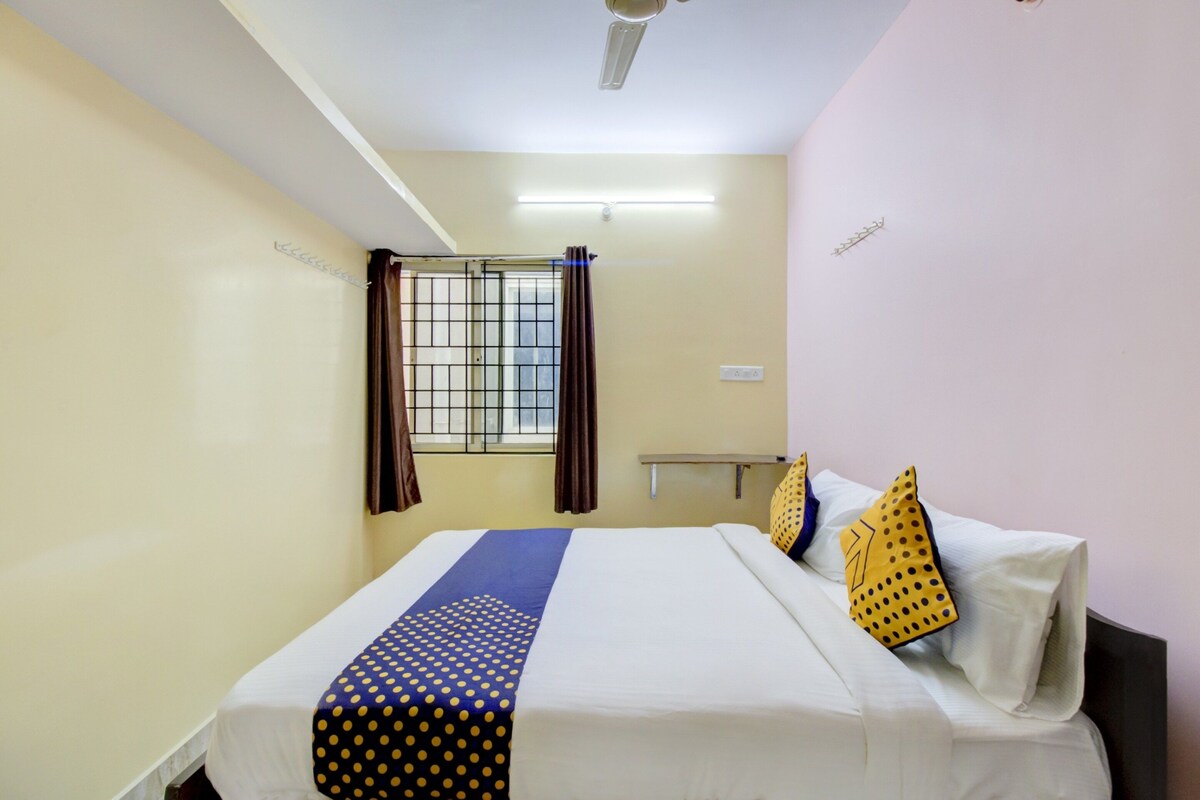 A hotel room with a bed, curtains, a window with bars, a ceiling fan, and a bedside table.