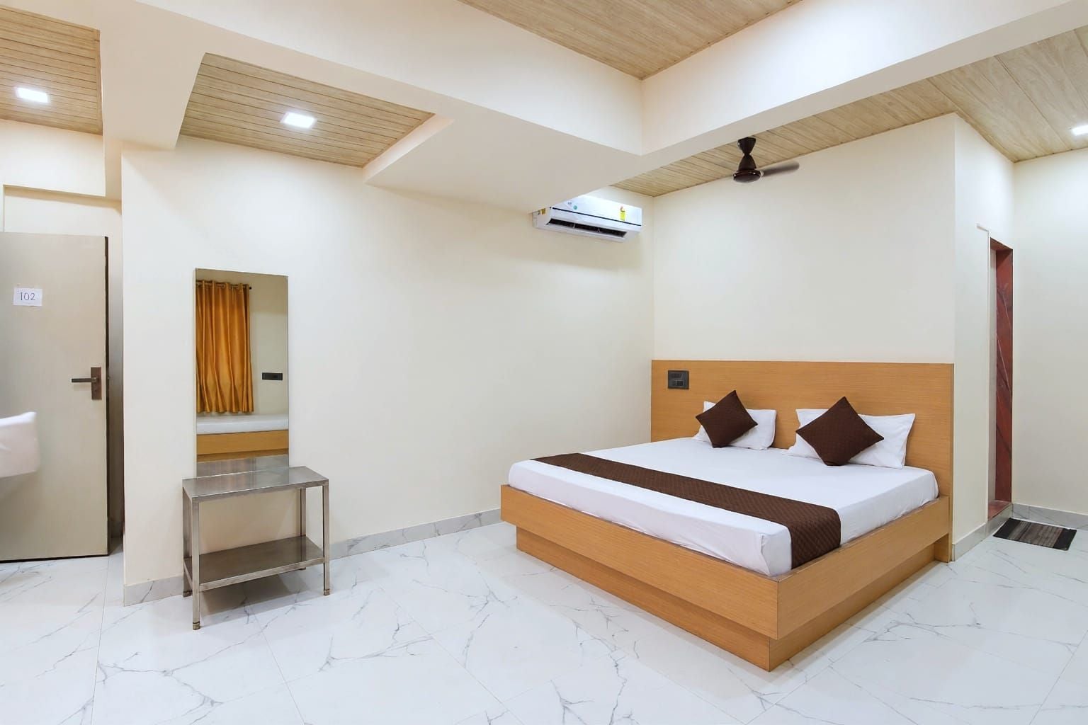 A hotel room with a bed, a bedside table, an air conditioning unit, and a ceiling fan.