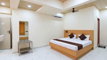 A hotel room with a bed, a bedside table, an air conditioning unit, and a ceiling fan.