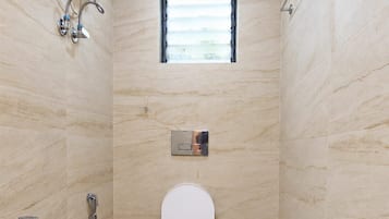 A small, tiled bathroom with a toilet, a shower, and a window.