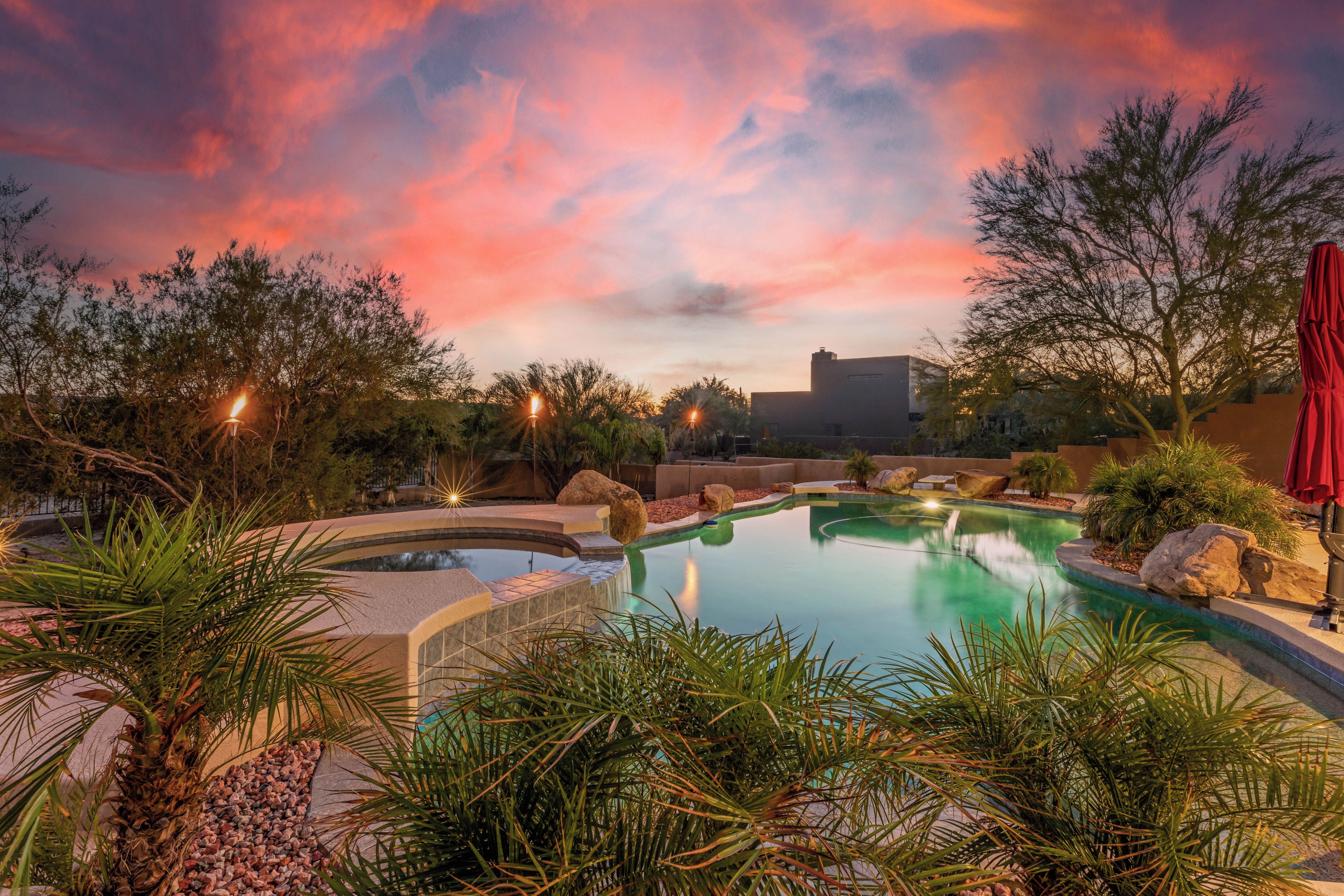 Una piscina con cascada, rodeada de plantas tropicales y un cielo al atardecer.