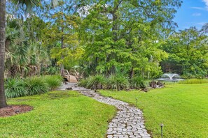A stone pathway leading through a lush garden with a wooden bridge and a fountain. - Golden Oaks Estate: Lagoon Pool, Treehouse, Private Lake & Acres of Waterfront Nature (Naples)