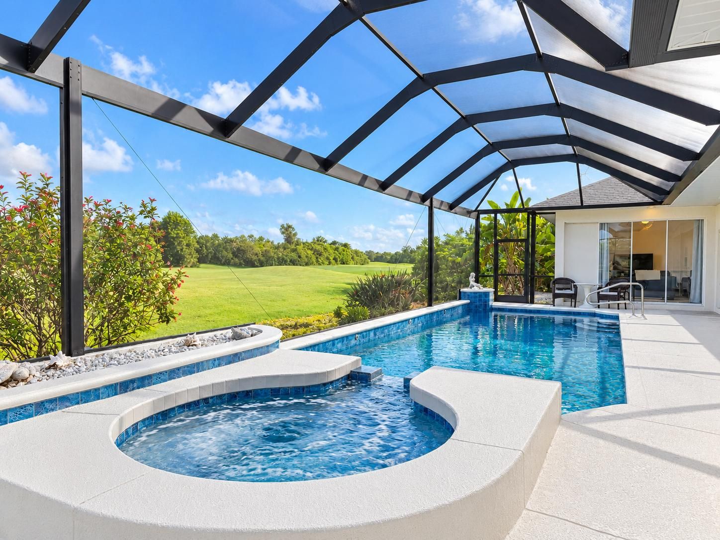 A covered outdoor swimming pool with a hot tub, surrounded by a patio area with a view of a golf course.