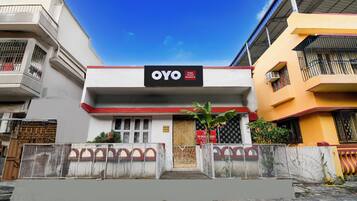 Un hotel llamado OYO con un letrero, una entrada protegida por una reja y un cielo azul despejado.