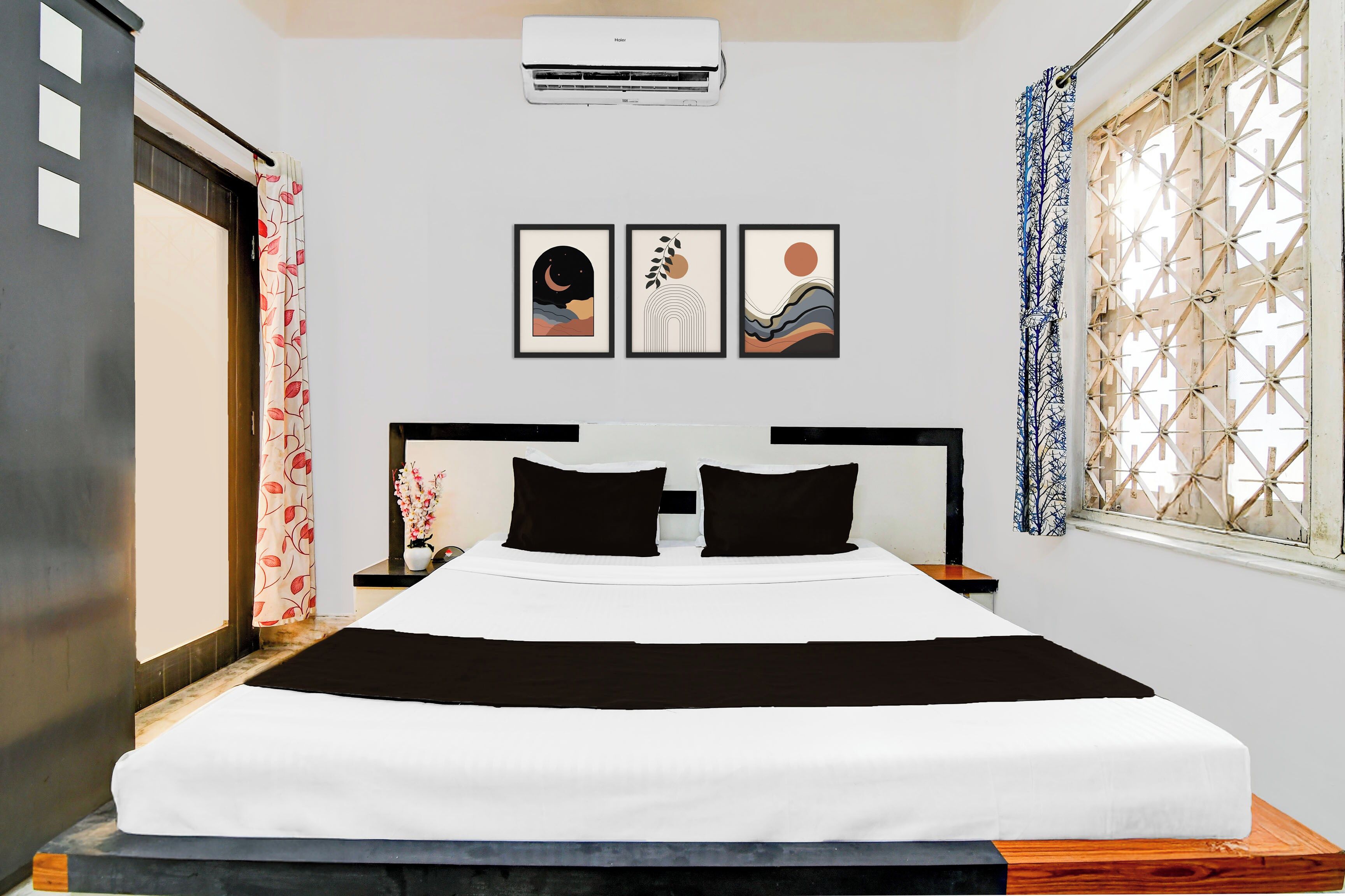 Habitación de hotel con cama, mesita de noche, aire acondicionado instalado en la pared y ventana con celosía decorativa.