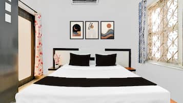Habitación de hotel con cama, mesita de noche, aire acondicionado instalado en la pared y ventana con celosía decorativa.