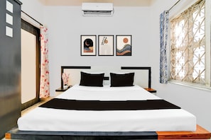 Quarto de hotel com cama, mesa de cabeceira, ar condicionado fixado na parede e janela com divisória decorativa.