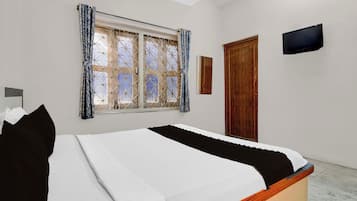 Un dormitorio con cama, ventana con cortinas, puerta y televisor de pantalla plana montado en la pared.