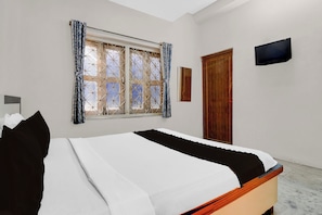Quarto com cama, janela com cortinas, porta e televisão de tela plana na parede.