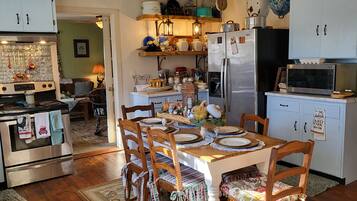 Une cuisine avec des meubles en bois, une table à manger pour quatre personnes, un réfrigérateur, un four à micro-ondes et un ventilateur de plafond.