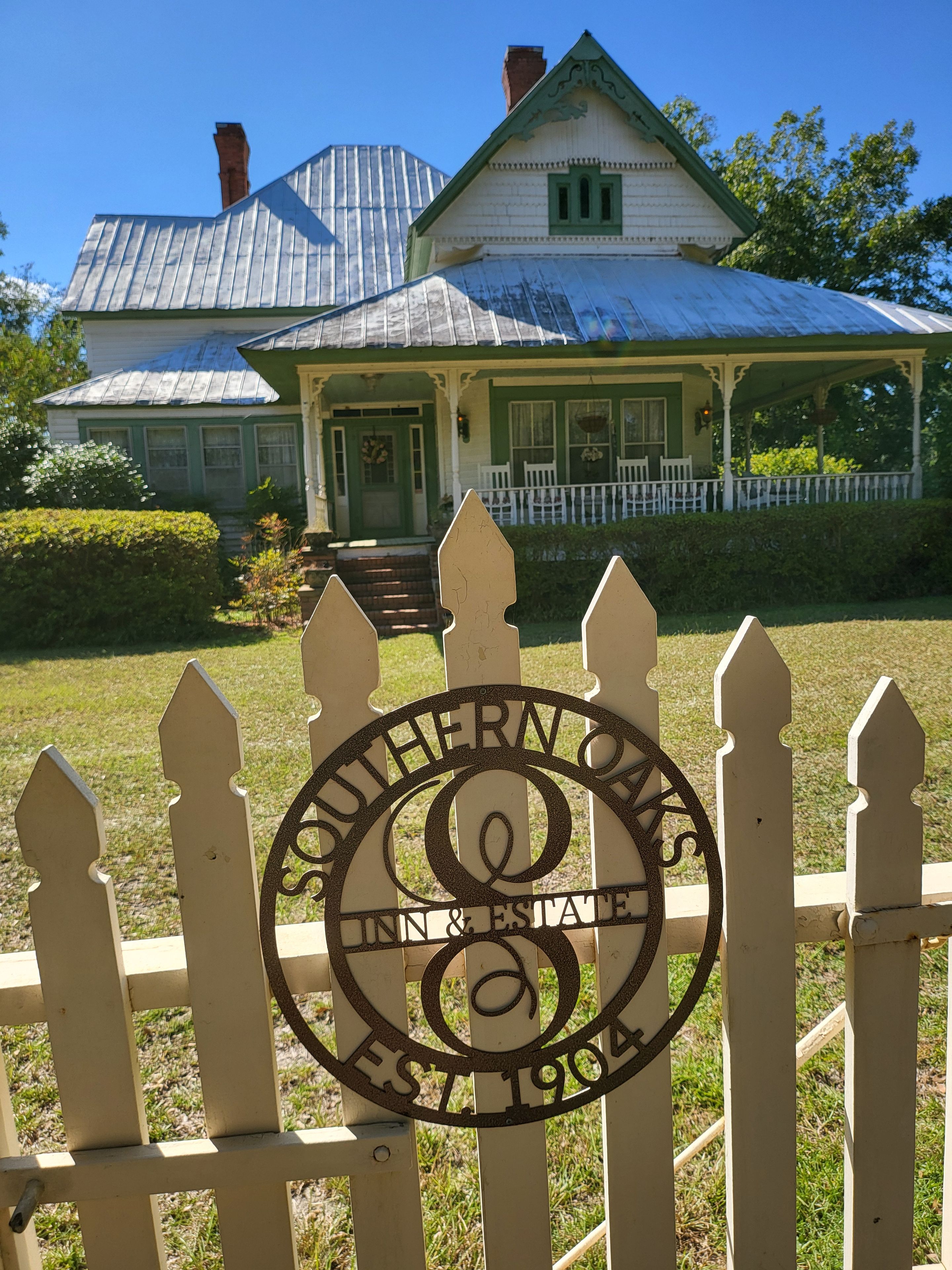 Une clôture blanche en bois, avec une plaque métallique indiquant « Southern Oaks Inn & Estate » et « Fondé en 1904 ».
