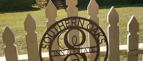 Una cerca blanca de piquetes con un letrero metálico que indica 'Southern Oaks Inn & Estate' y 'Fundado en 1904'.