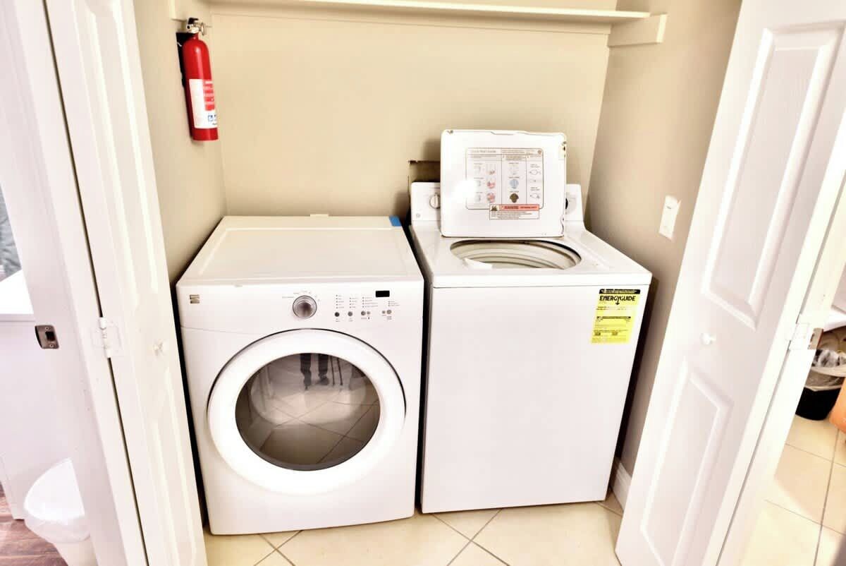 A laundry area with a washing machine and dryer, a fire extinguisher on the wall, and a door leading to another room.