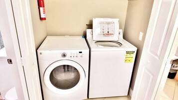 A laundry area with a washing machine and dryer, a fire extinguisher on the wall, and a door leading to another room.