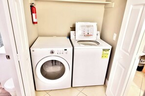 A laundry area with a washing machine and dryer, a fire extinguisher on the wall, and a door leading to another room. - 2BR Balcony Pool Gym Near Las Vegas Strip (Las Vegas)