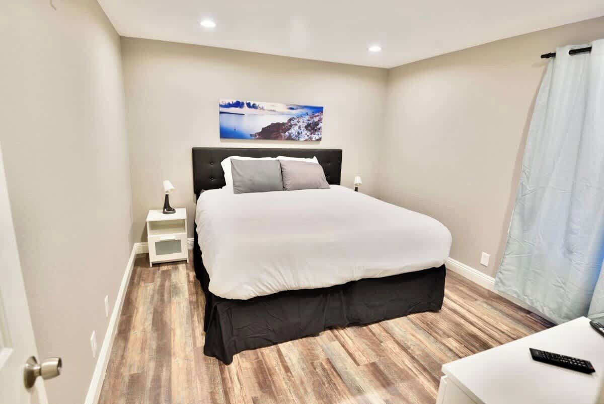 A bedroom with a large bed, a nightstand, a remote control, and a painting on the wall.