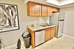 A kitchen with wooden cabinets, a stainless steel dishwasher, a refrigerator, a sink, and a trash bin. - 2BR Balcony Pool Gym Near Las Vegas Strip (Las Vegas)